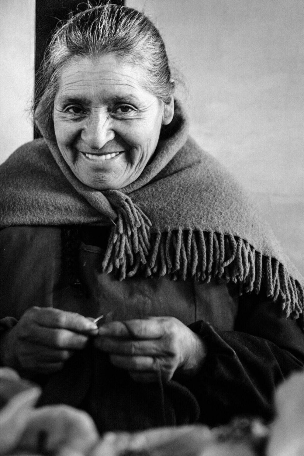 A respectful, character-rich portrait of an elderly market vendor with a warm smile, surrounded by her goods