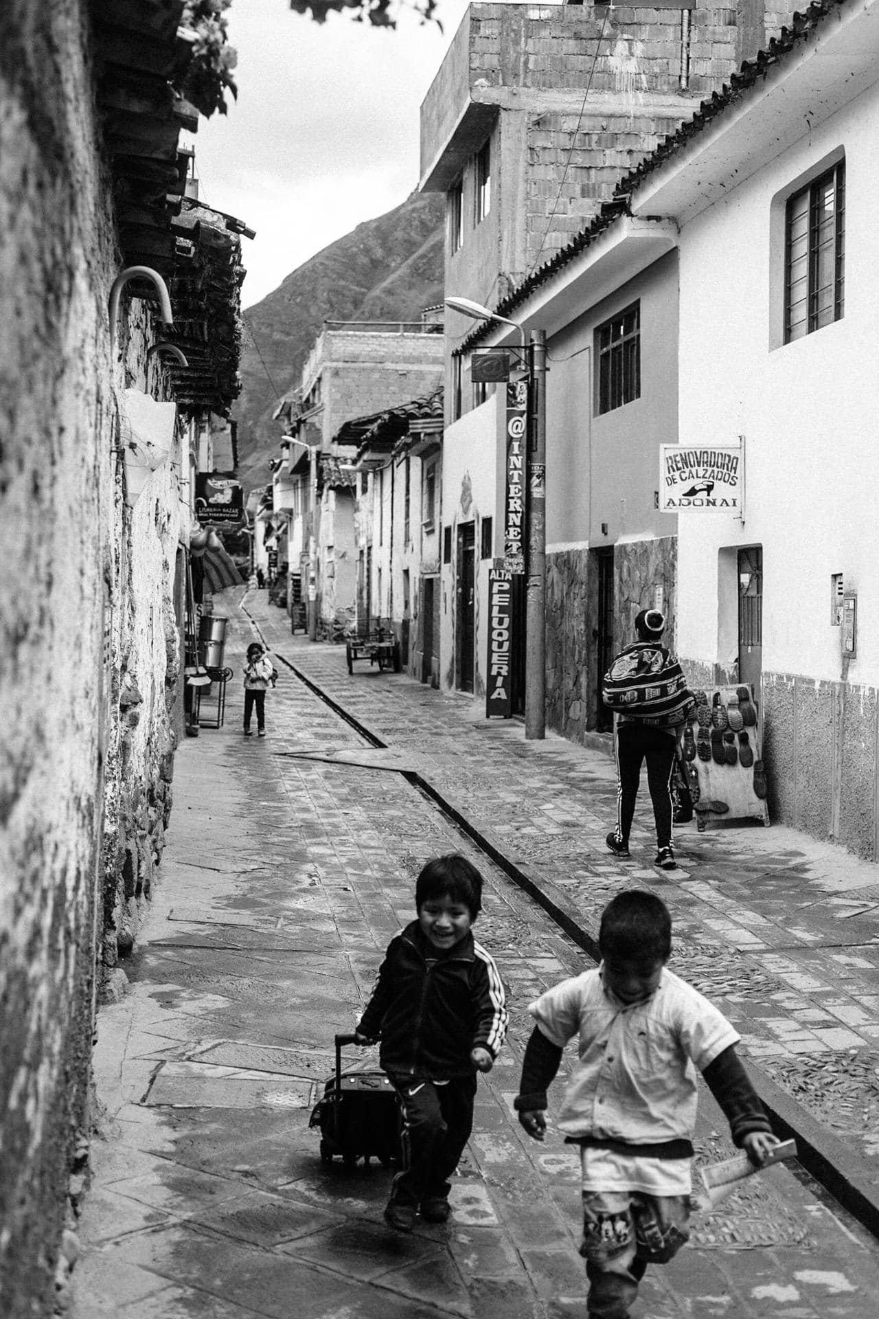 A dynamic, candid shot of two children laughing and running in a plaza, with historic architecture in the background cusco street photography