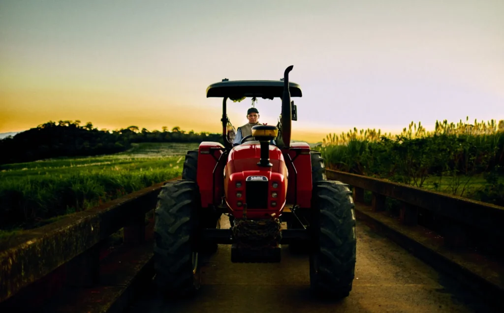 Red tractor driving along a rural road between green fields at sunset in Costa Rica