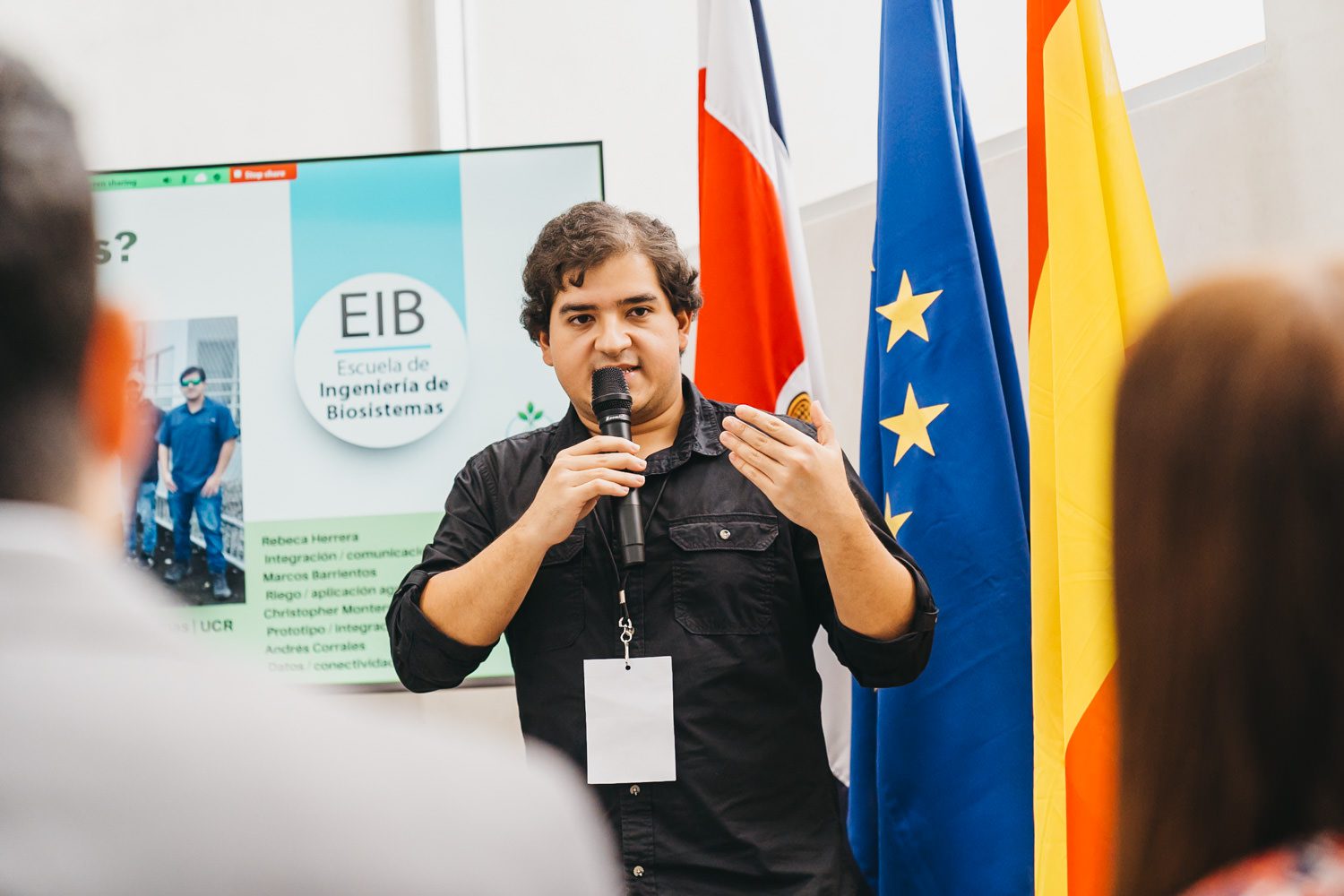 Participant speaking beside monitors and event displays at the Central American 5G Innovation Hackathon in Costa Rica